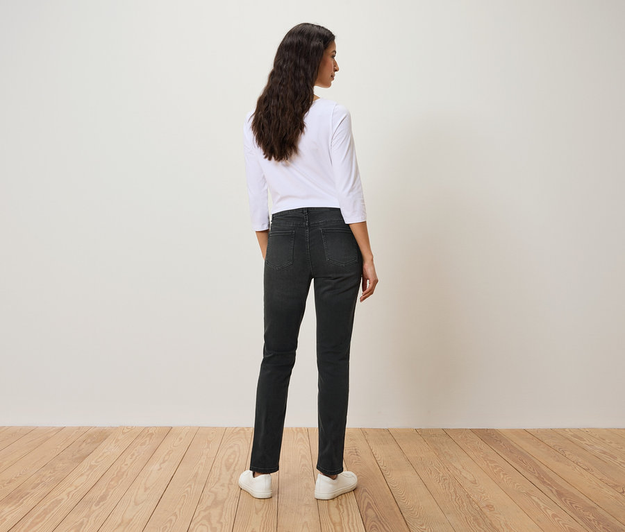 Vue de dos d'une femme aux cheveux ondulés foncés portant un t-shirt blanc à manches trois-quarts, un jean noir et des chaussures blanches.