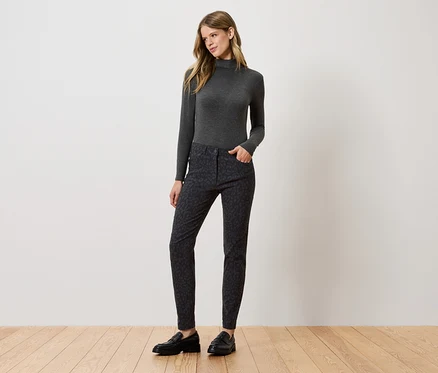 Une femme debout posant dans un col roulé gris, un pantalon à motifs et des chaussures noires.