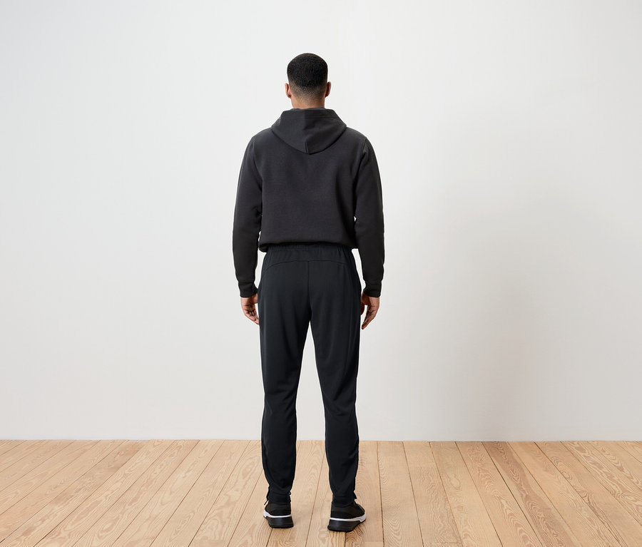 Un homme vu de dos porte un pantalon noir et un sweat à capuche.