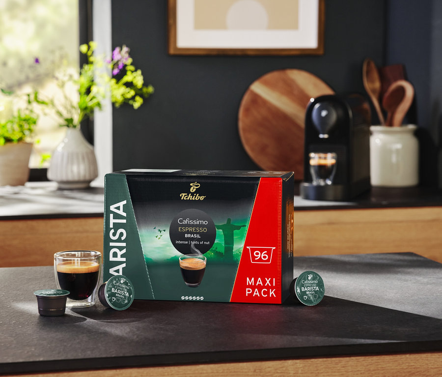 Sur une table se trouvent un paquet de capsules Espresso Brasil, un verre d'espresso et une machine à café.