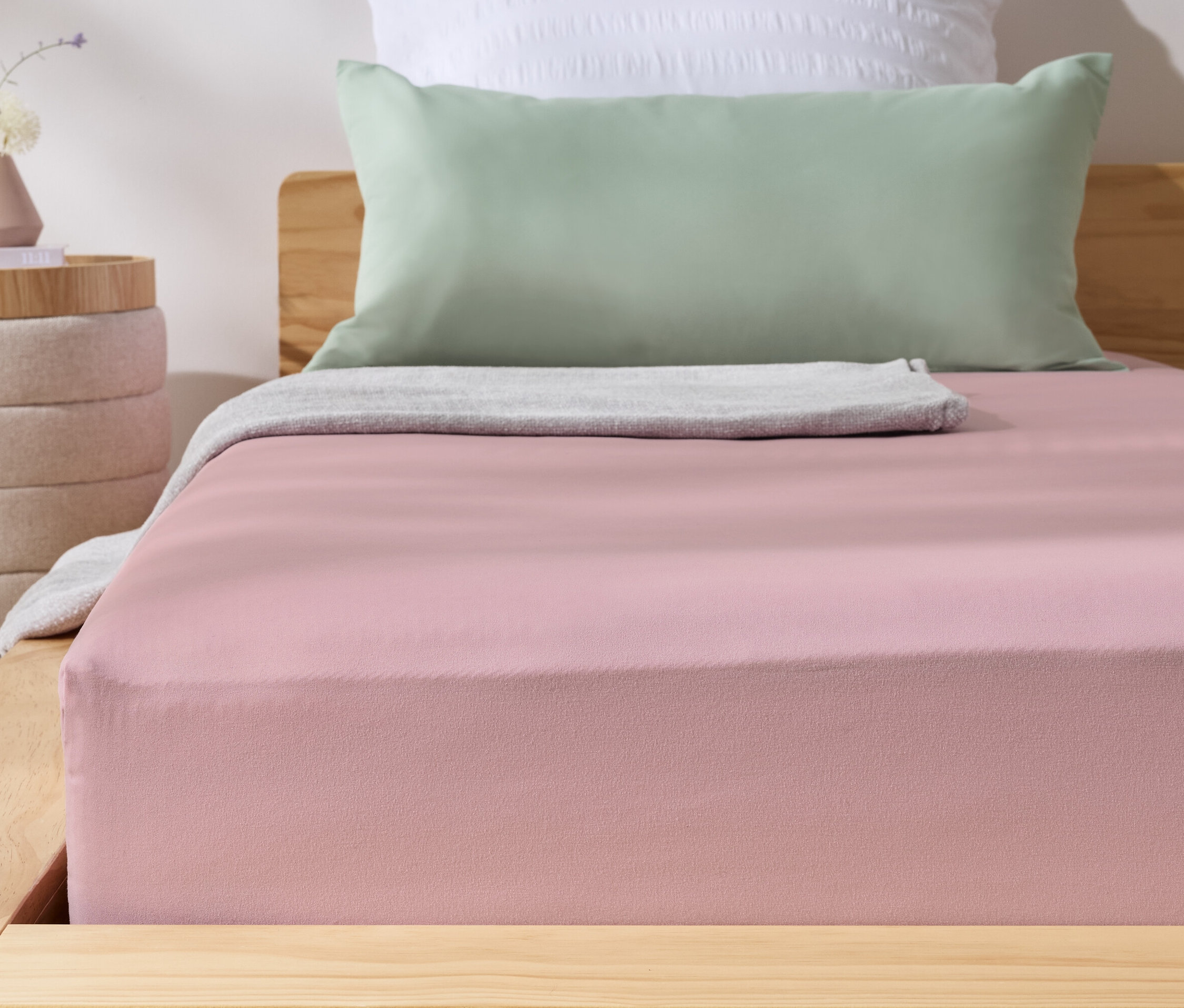 Drap-housse rose en microfibre sur un lit. À côté se trouve une table de chevet avec un vase.