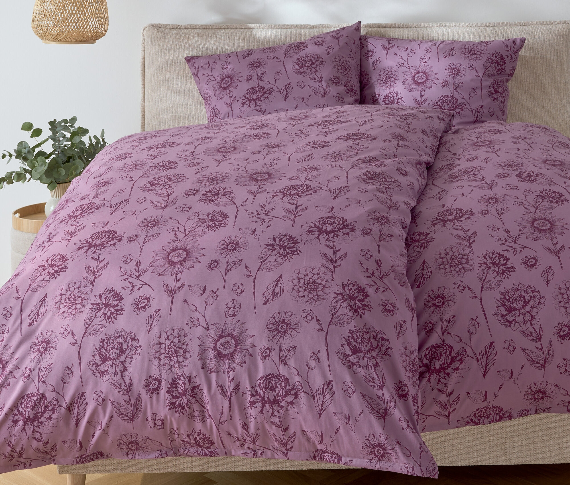 Chambre avec un lit avec des draps à fleurs violets et deux oreillers.