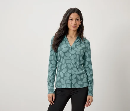 Une femme porte un chemisier turquoise à motifs et un pantalon noir.