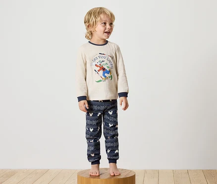 Un garçon se tient sur un socle en bois et porte un pyjama Disney.