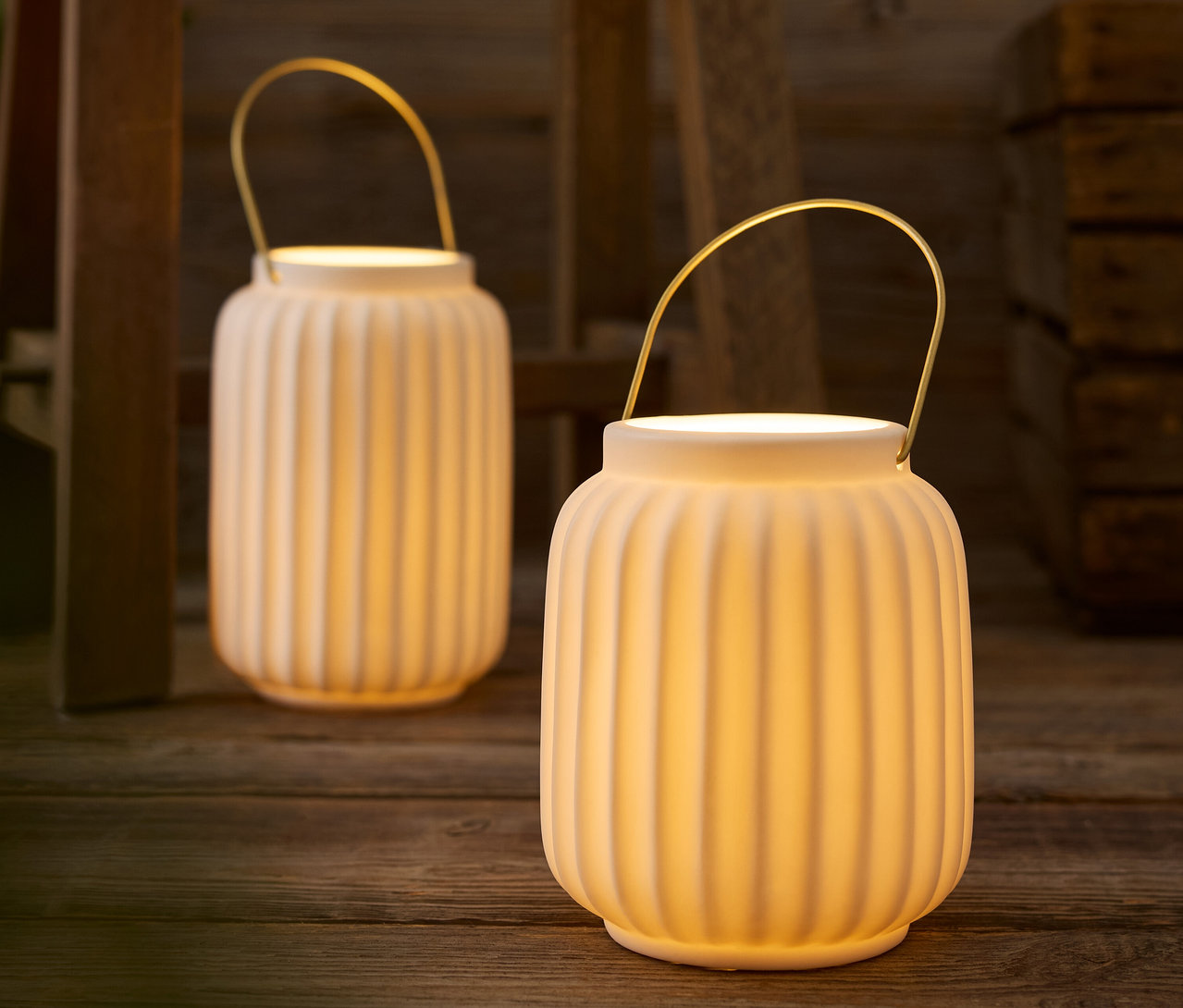Deux lanternes blanches avec des poignées dorées posées sur une table en bois.