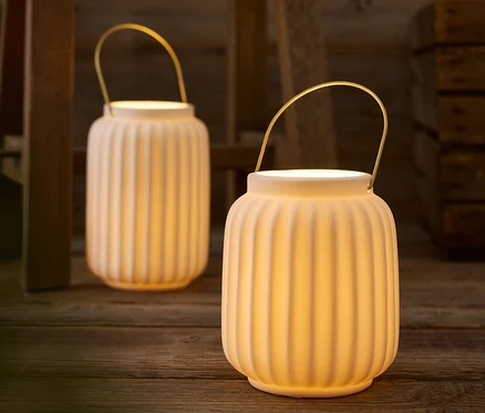 Deux lanternes blanches avec des poignées dorées posées sur une table en bois.