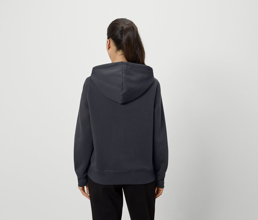 Une femme, vue de dos, porte un sweat à capuche gris foncé et un pantalon noir.