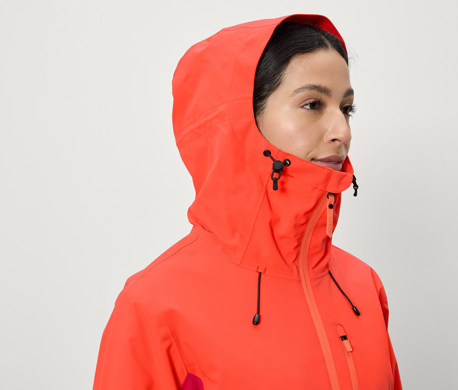 Une femme porte une veste corail avec une capuche.