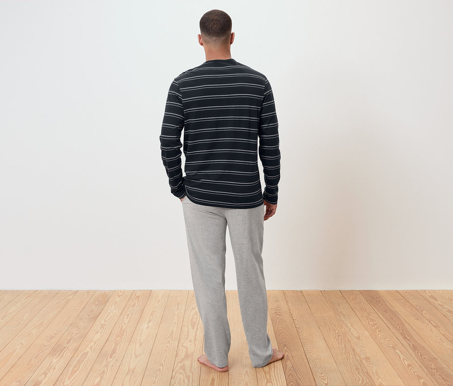 Un homme, de dos, porte un t-shirt rayé à manches longues et un pantalon de survêtement gris.