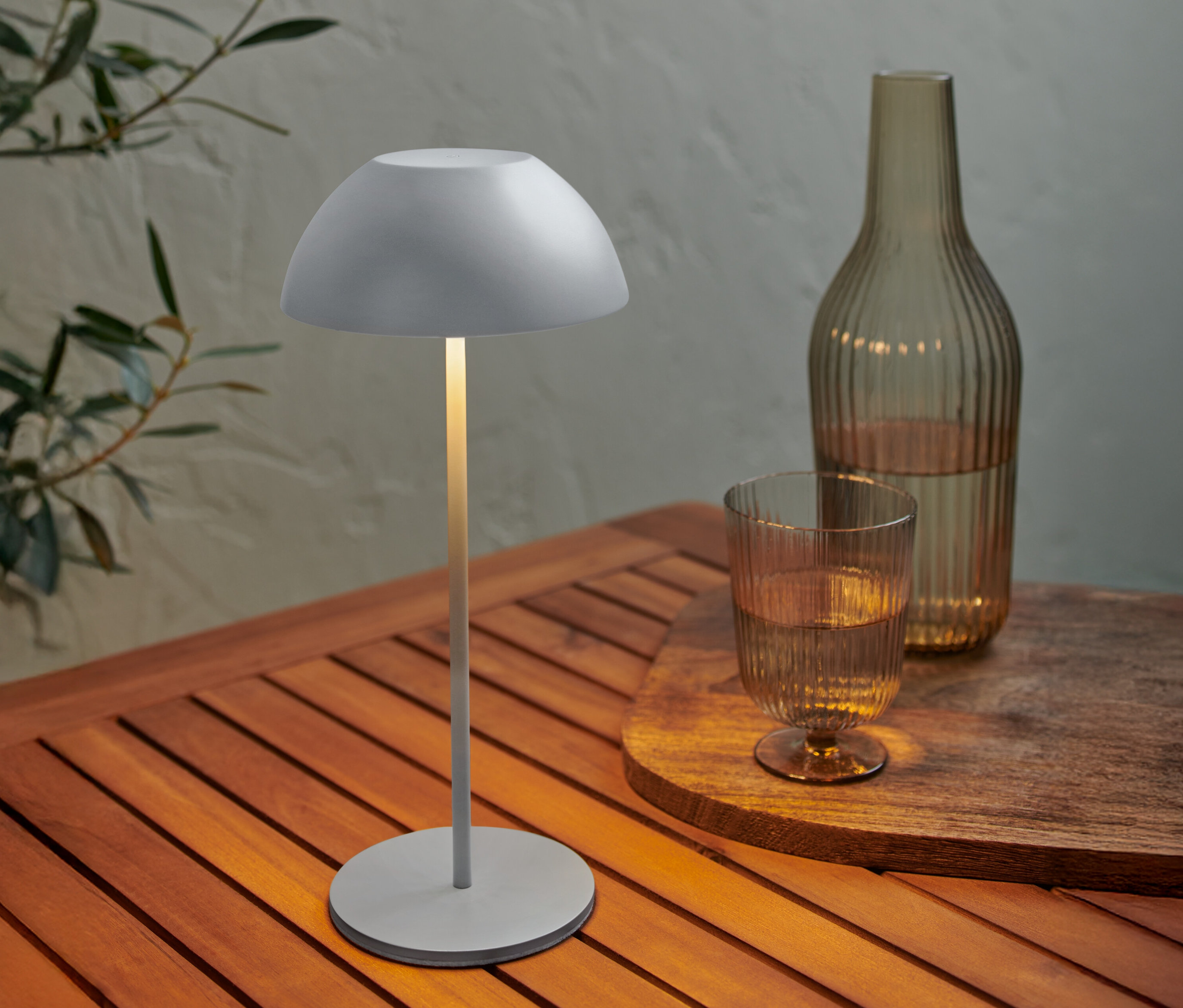 Une lampe grise est posée sur une table en bois à côté d'une bouteille et d'un verre d'eau.
