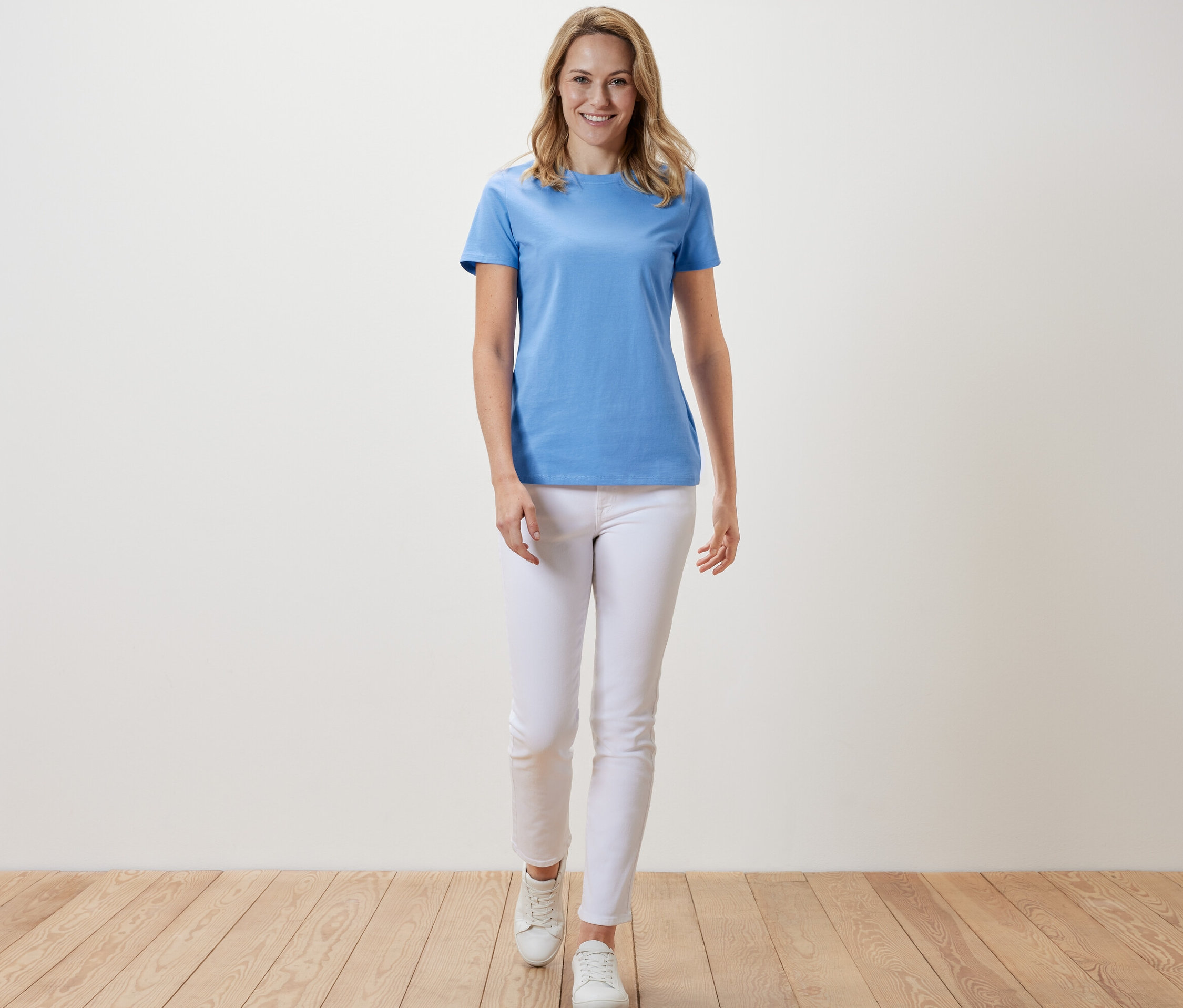Une femme avance et porte un t-shirt basique bleu clair et un pantalon blanc.