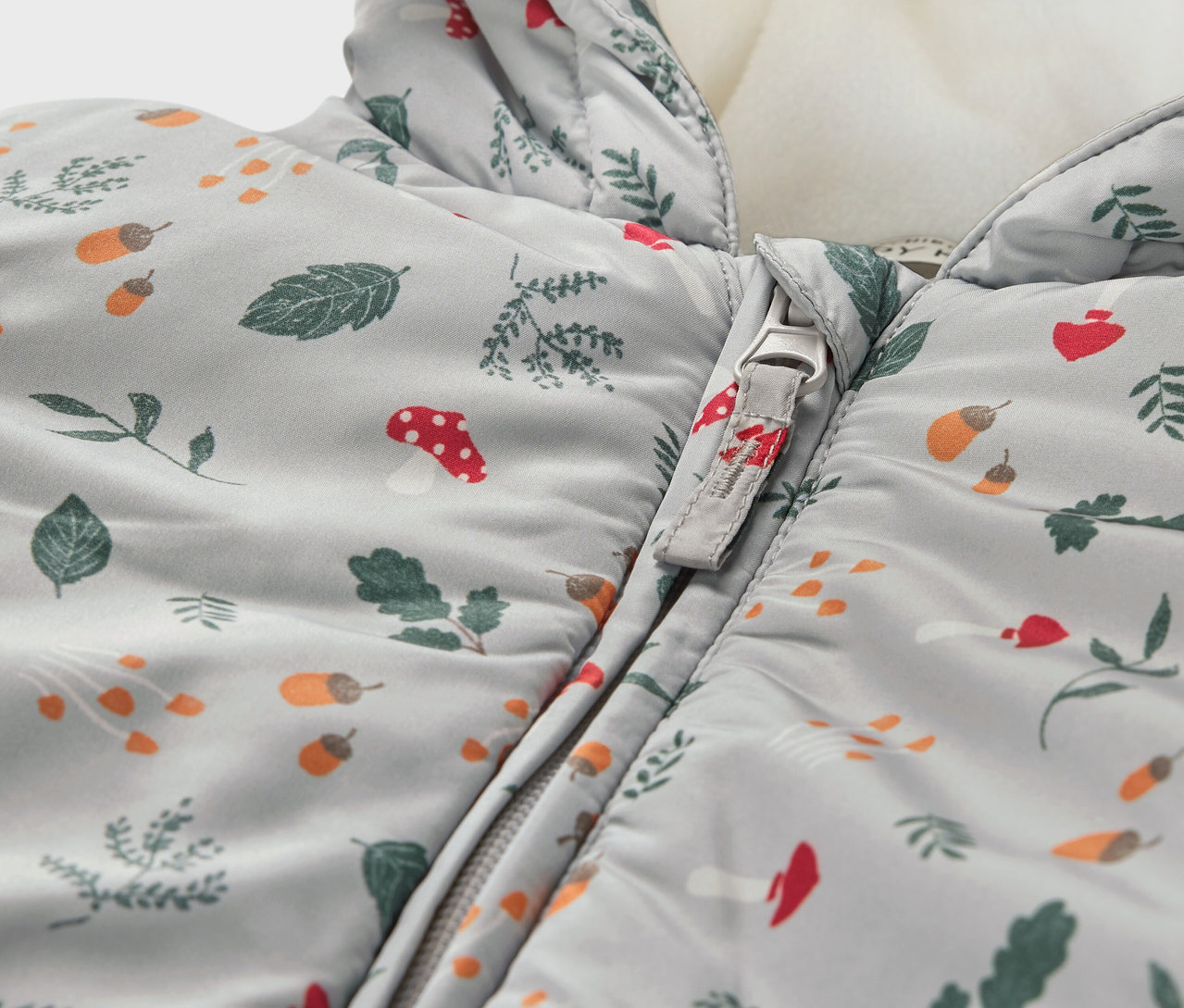 Gros plan sur une combinaison d’hiver pour bébé avec un motif de feuilles, de champignons et de glands.