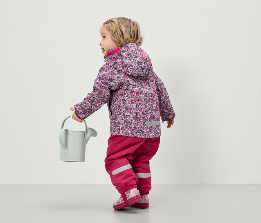 Un enfant avec une veste à fleurs et un pantalon rose tenant un arrosoir.