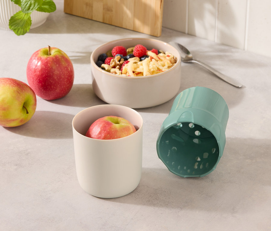 Deux pommes à côté d'un bol de muesli et d'un gobelet avec une pomme et un gobelet bleu.