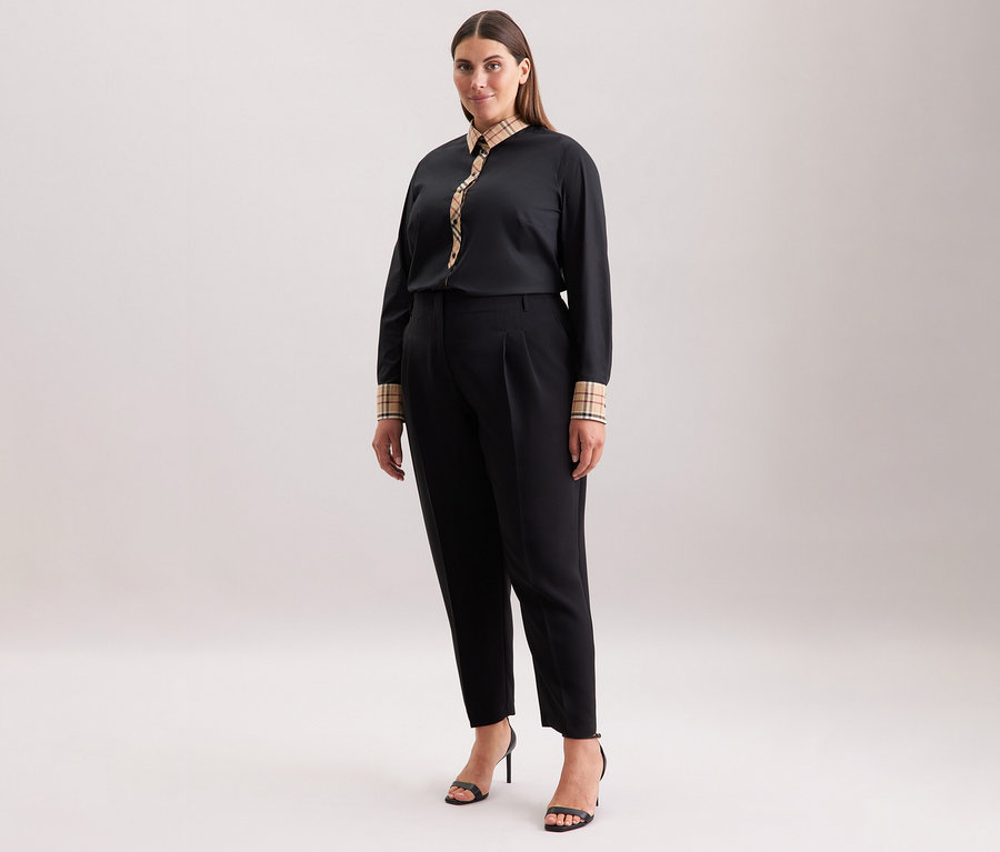 Femme portant un pantalon noir et un chemisier en popeline à carreaux Seidensticker et des talons hauts noirs.