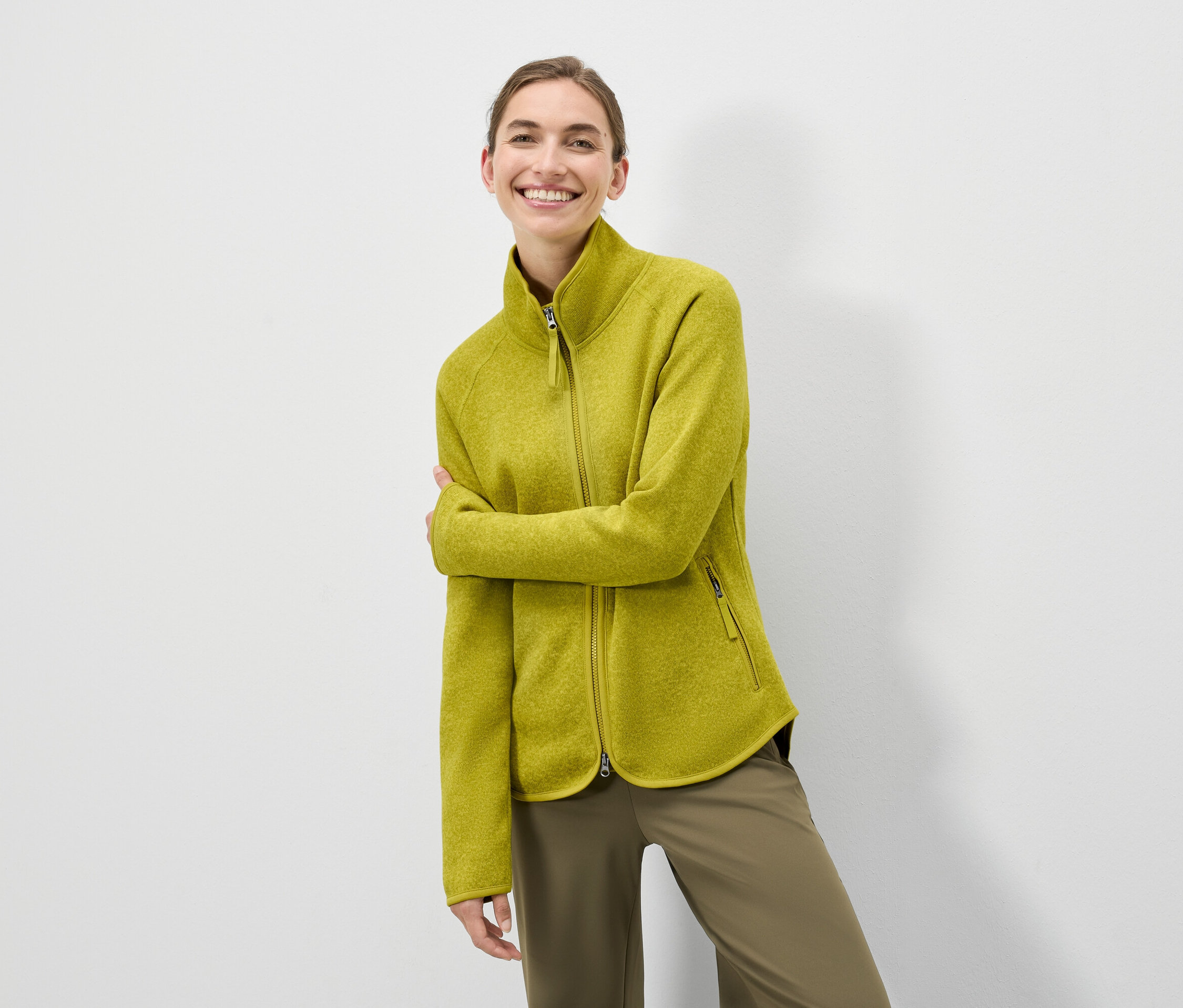 Une femme pose en veste en polaire vert olive zippée et pantalon vert olive.