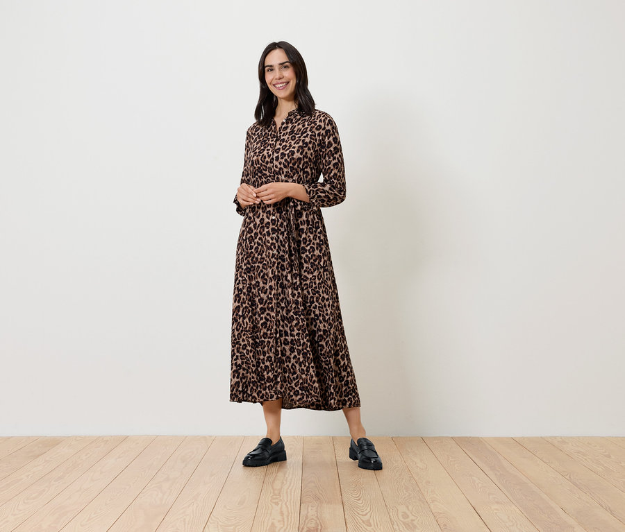 Une femme pose dans une robe à motifs à manches longues et des chaussures noires.