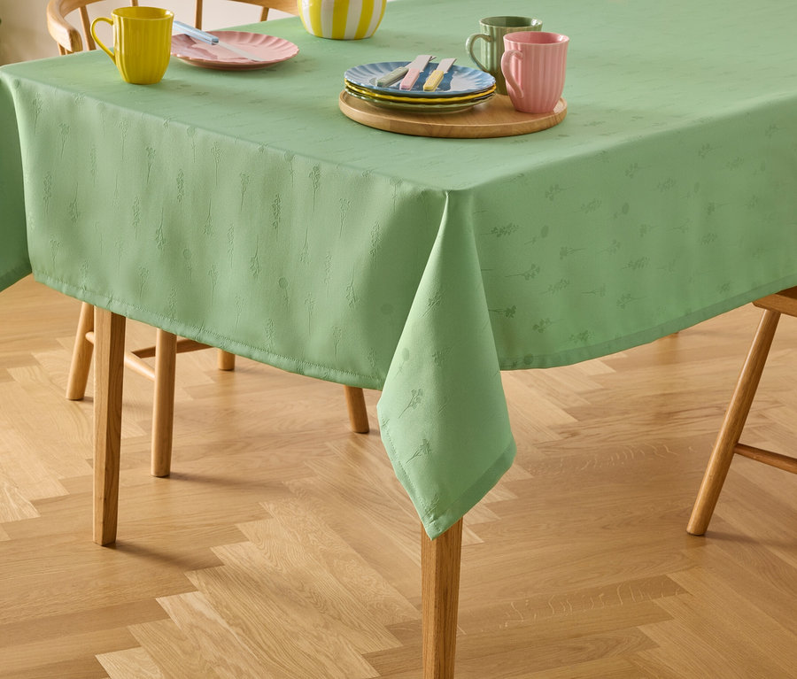 Nappe verte à motifs floraux sur une table en bois avec des chaises, avec des assiettes et des tasses dessus.