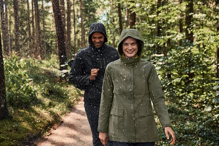 Deux personnes marchent sous la pluie dans la forêt. La femme porte un pull camionneur en polaire kaki-anthracite.