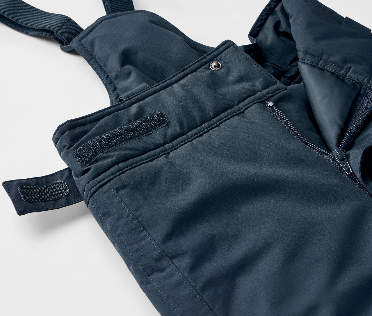 Gros plan sur un pantalon à bretelles bleu avec fermeture éclair et velcro.