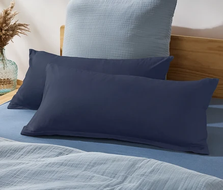 Deux oreillers bleu marine sur un lit bleu avec une couverture bleu clair et un vase avec de l'herbe de pampa.