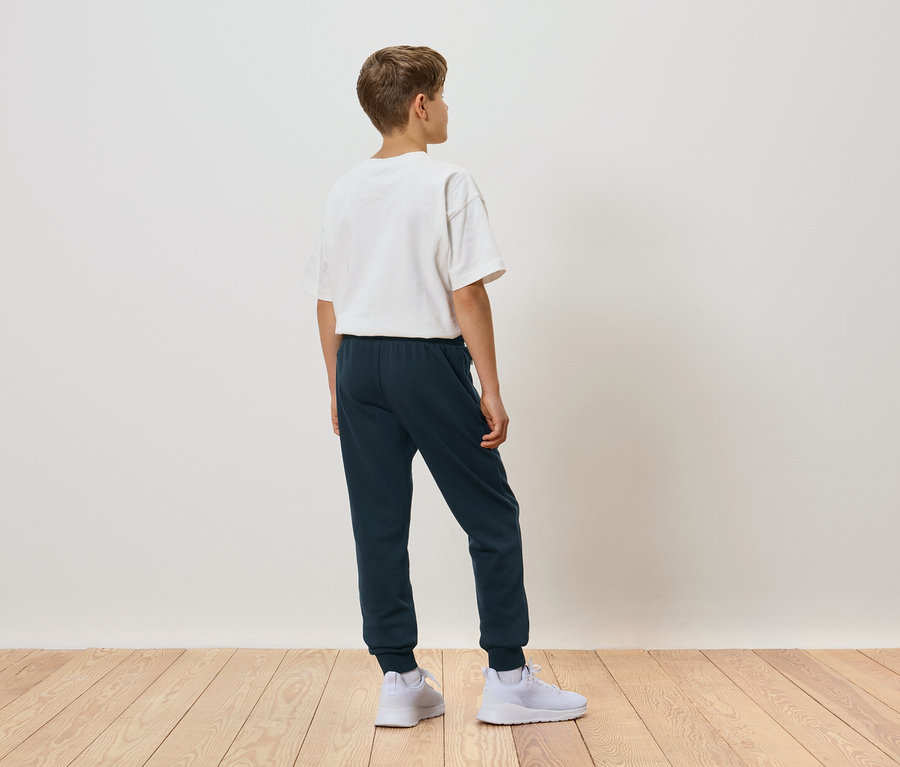 Garçon vu de dos portant un t-shirt blanc, un pantalon de jogging bleu et des baskets blanches.