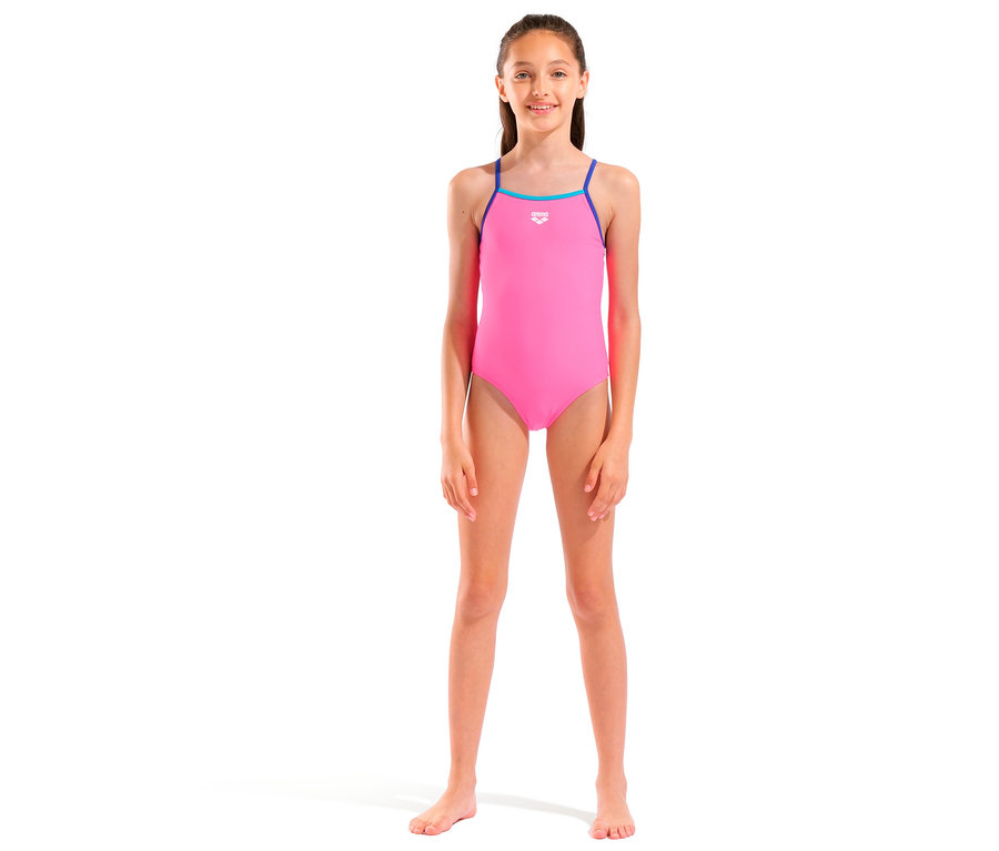 Fille debout pieds nus dans un maillot de bain rose avec des bretelles bleues sur fond blanc.