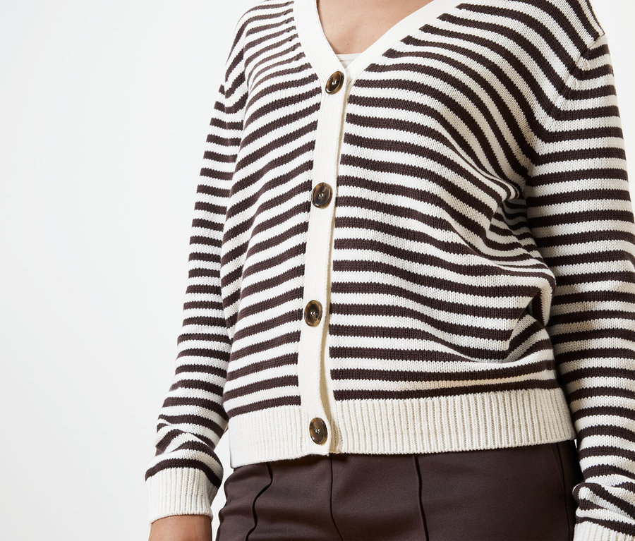 Haut du corps d'une personne portant un cardigan rayé marron et blanc avec des boutons marron et un pantalon marron sur fond blanc.