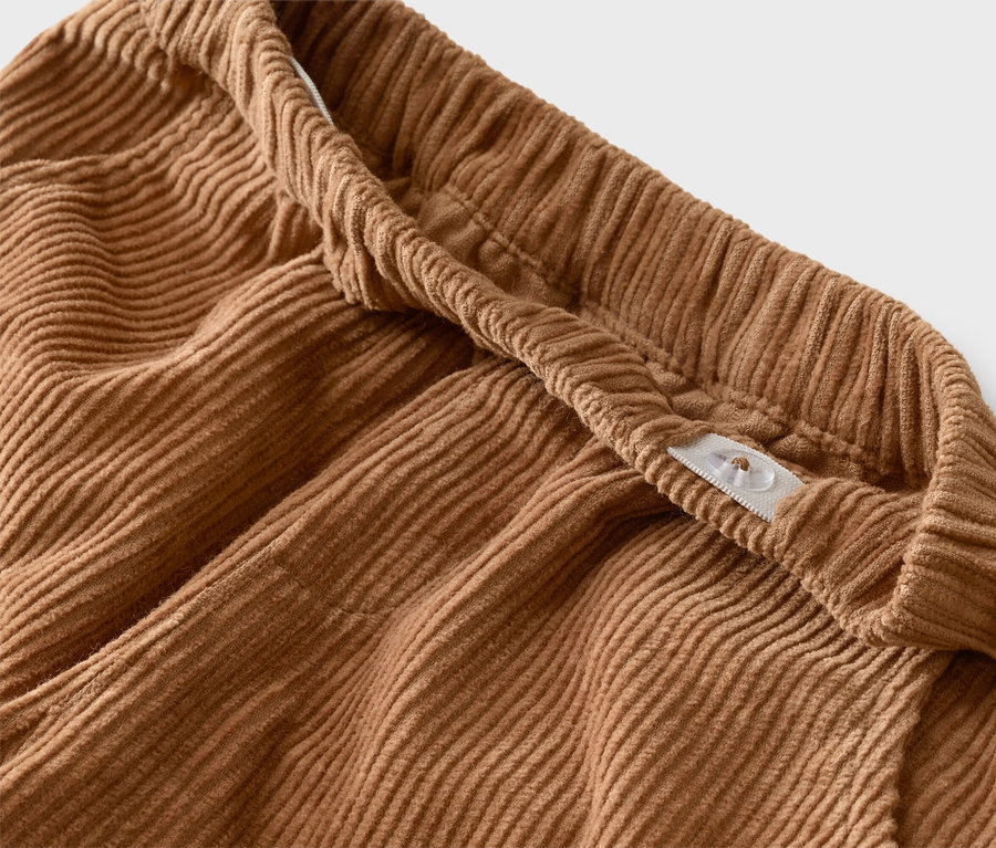 Gros plan d'un pantalon en velours côtelé marron avec une taille élastique et un bouton réglable.
