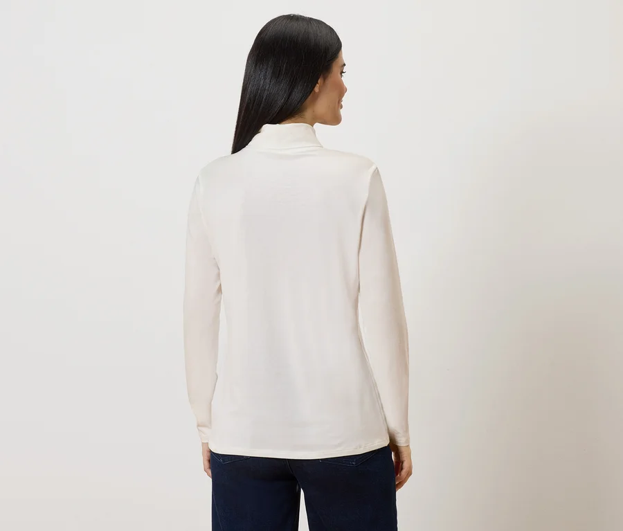Vue arrière d'une femme aux longs cheveux foncés portant un pull à col roulé crème et un jean foncé.