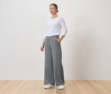 Femme portant un haut blanc, un pantalon gris rayé à jambes larges et des baskets blanches.