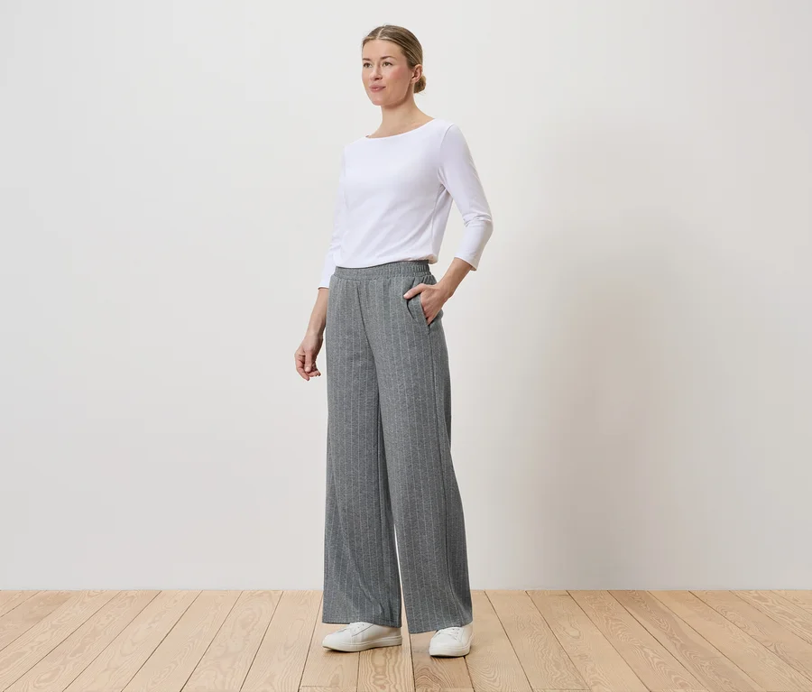 Femme portant un haut blanc, un pantalon gris rayé à jambes larges et des baskets blanches.