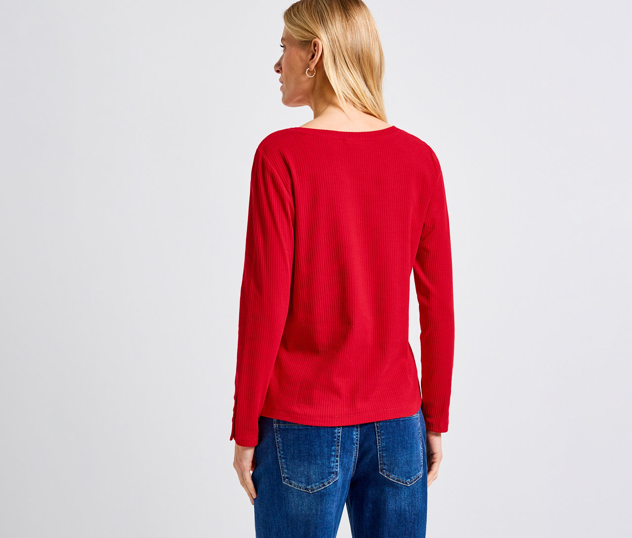 Une femme blonde vue de dos portant un maillot côtelé Street One rouge et un jean.