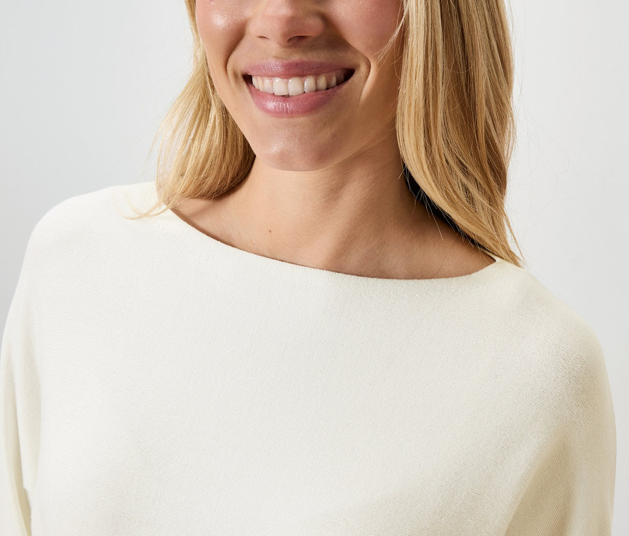 Une femme souriante porte un pull crème.