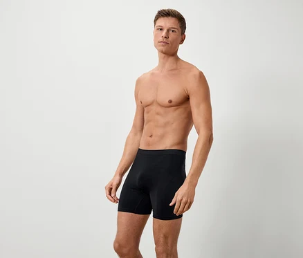 Un homme torse nu pose sur un fond blanc, vêtu d'un boxer noir.