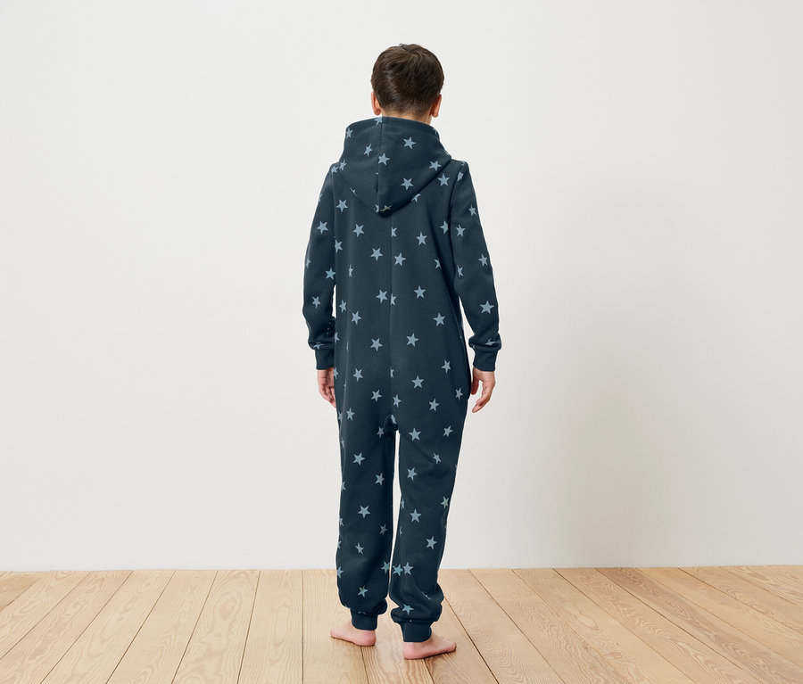 Un enfant, vu de dos, porte une combinaison à capuche bleu foncé à motifs étoilés.