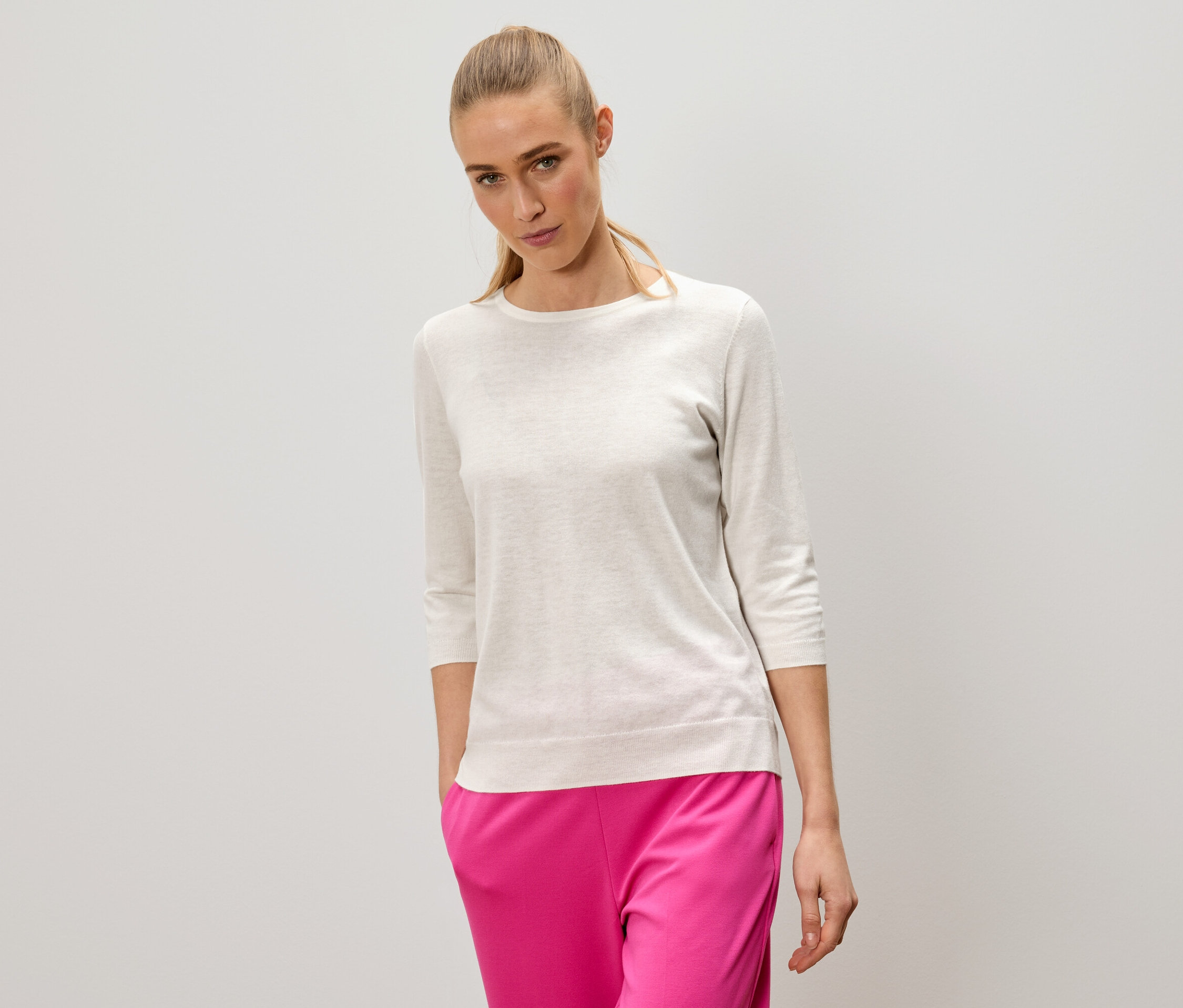 Une femme blonde porte un pull clair et un pantalon rose.