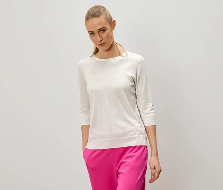 Une femme blonde porte un pull clair et un pantalon rose.