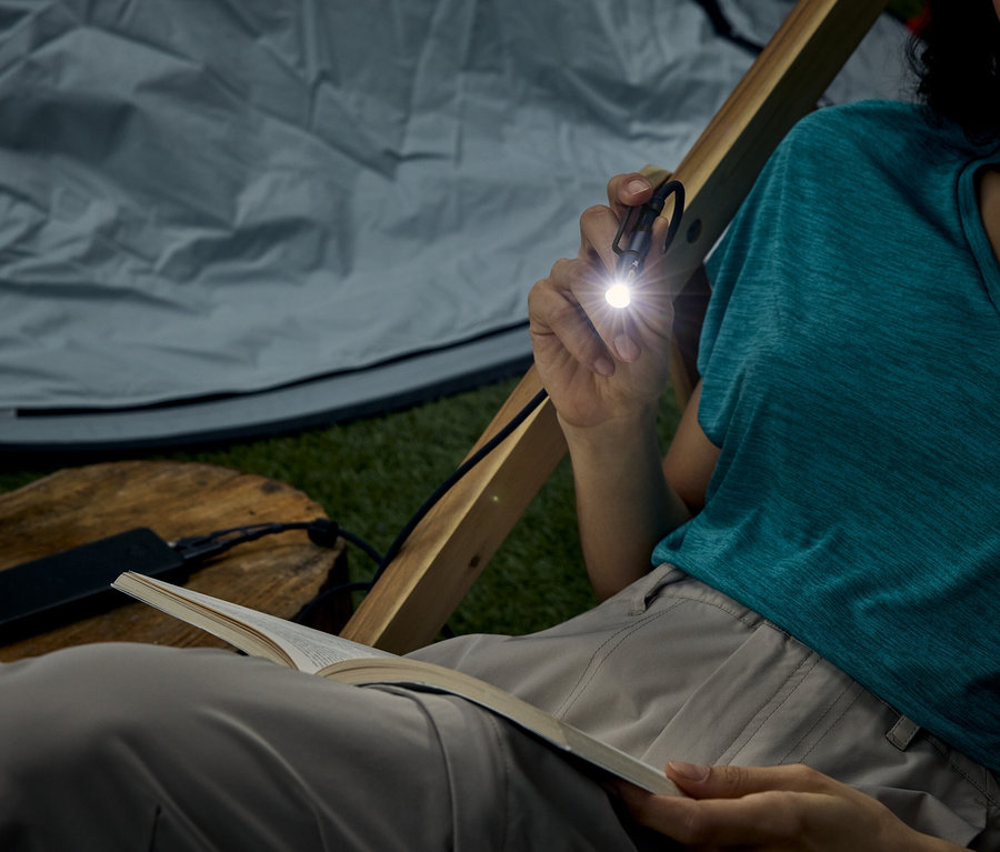 Femme assise dans une tente, lisant un livre avec une petite lampe de poche qu'elle tient.