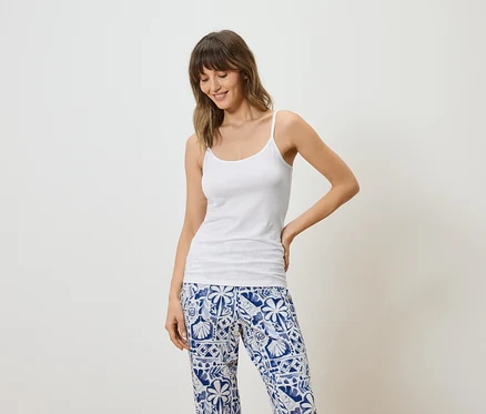 Femme portant un débardeur blanc et un pantalon à motifs bleus et blancs sur fond blanc.
