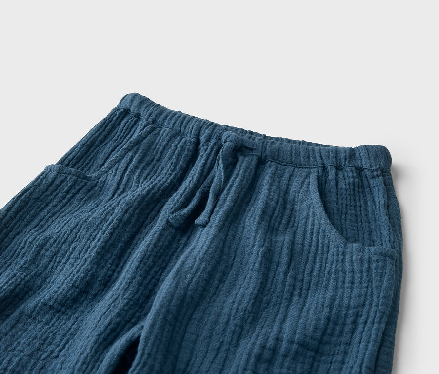 Gros plan sur un pantalon bleu en mousseline avec cordon de serrage et poches.