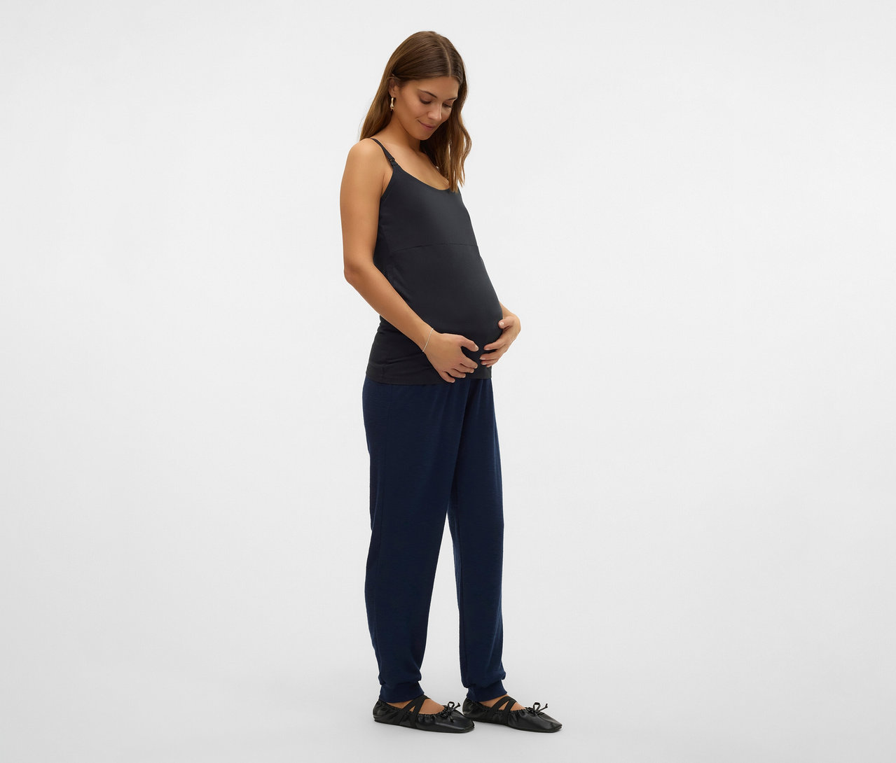 Femme enceinte de profil portant un des 2 tops à bretelles spaghetti MAMALICIOUS «
MLKERRIE
», un pantalon et des ballerines.