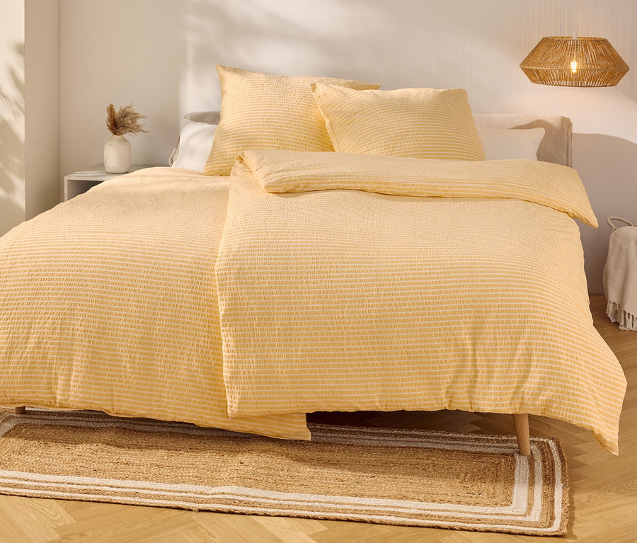 Des draps jaunes rayés recouvrent un lit avec deux oreillers. Un tapis est posé devant.