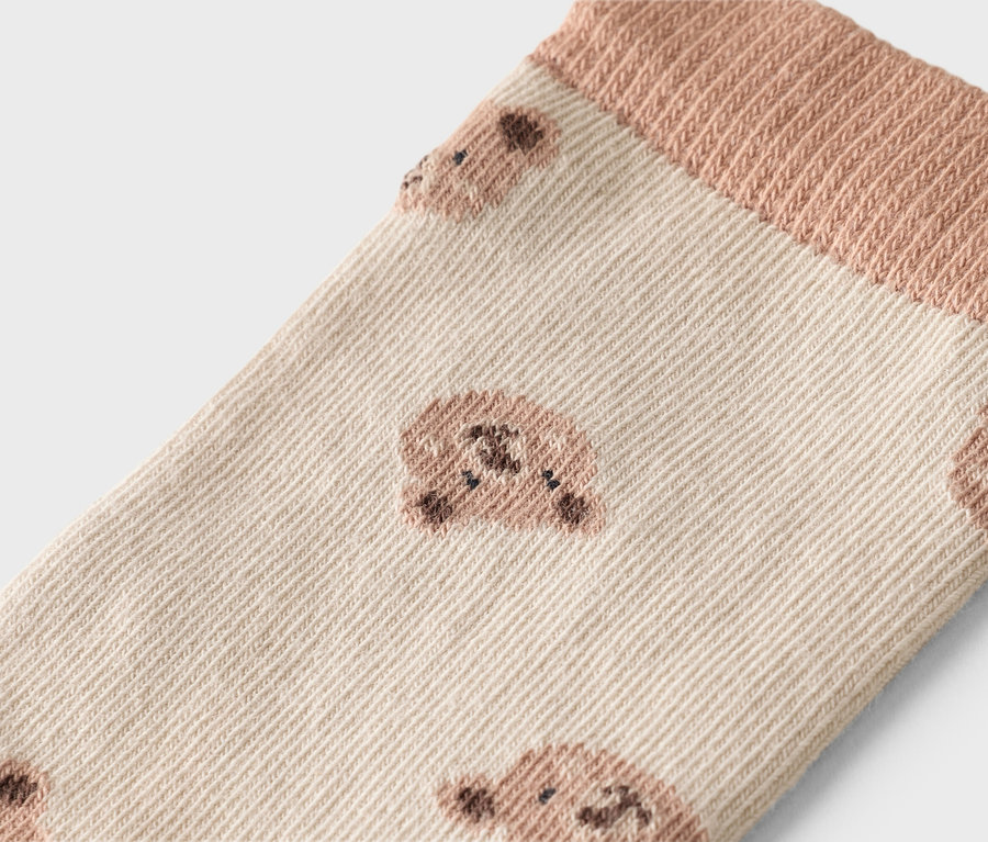 Gros plan d'une chaussette marron clair avec un motif d'ours et une bordure côtelée.