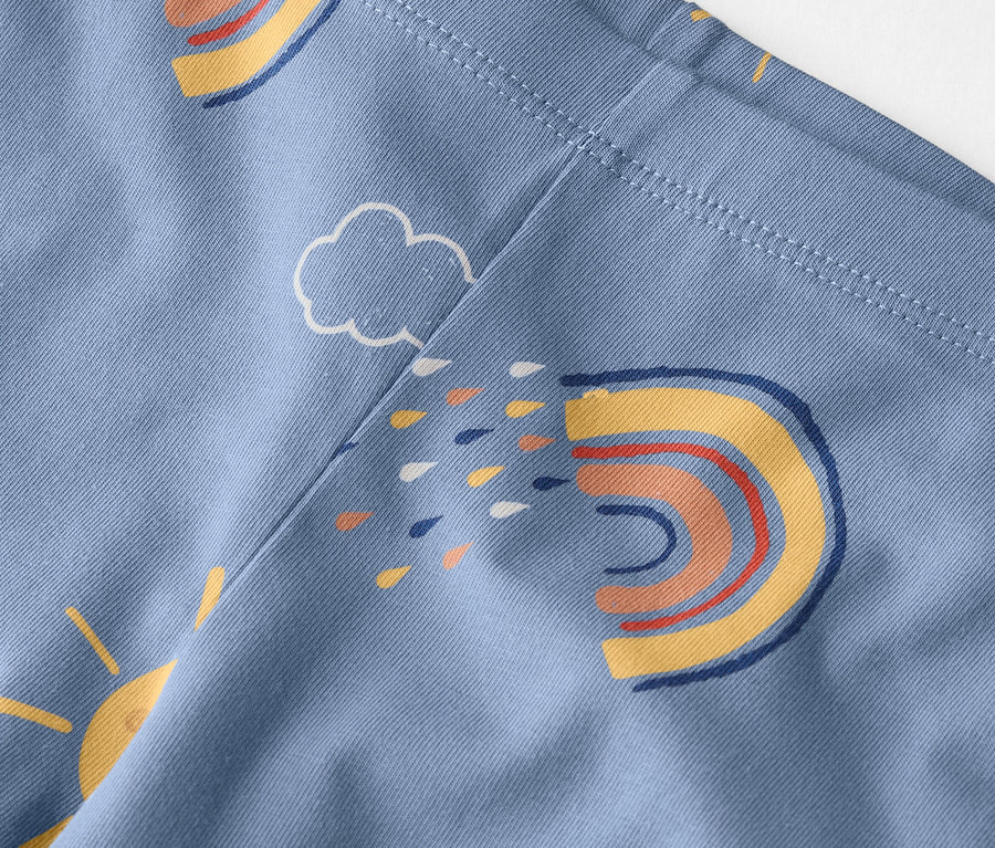 Gros plan d'un tissu bleu clair avec un motif d'arcs-en-ciel, de soleils et de nuages.