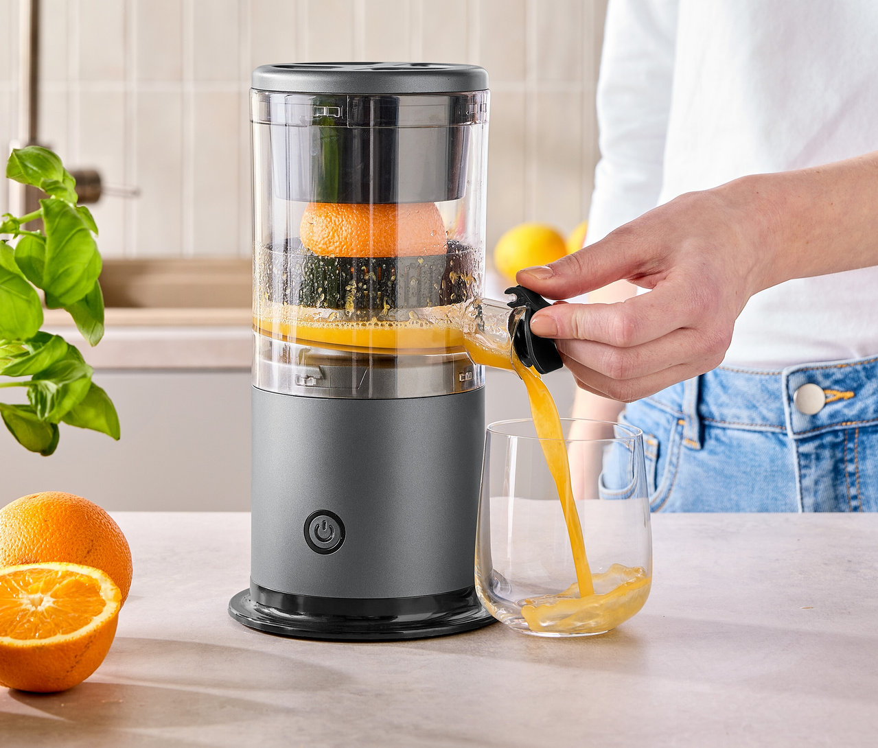Une femme verse du jus d'orange d'un presse-agrumes gris dans un verre.