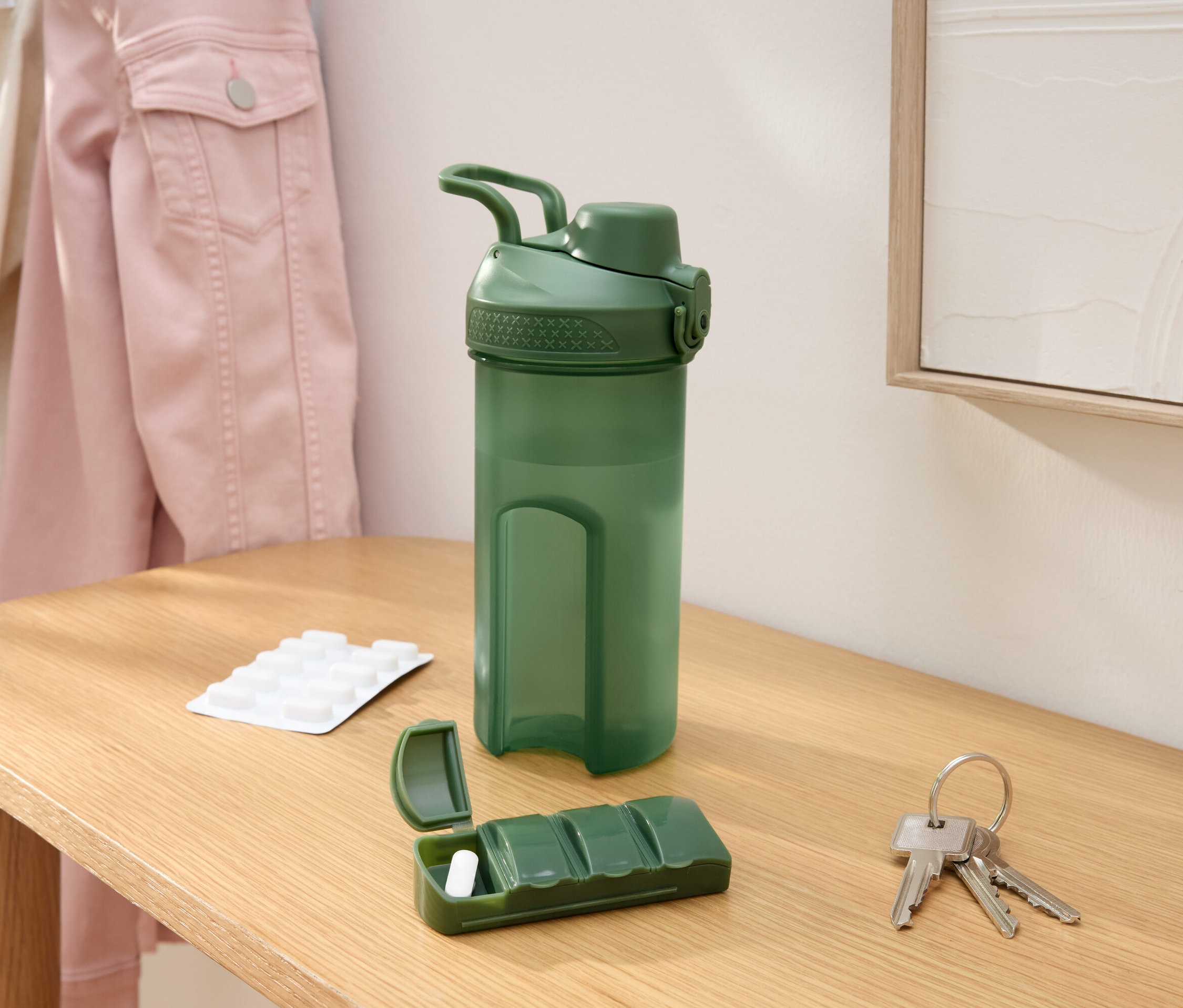 Bouteille d'eau verte, pilulier avec un comprimé, clés et blister sur une table.