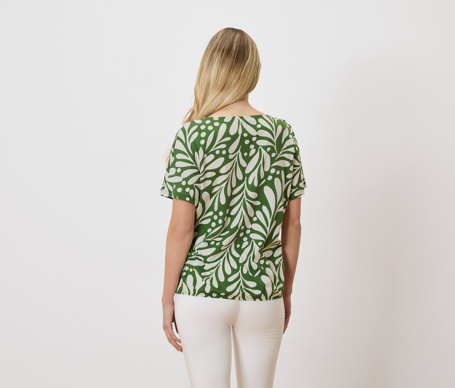 Vue de dos d'une femme blonde portant un haut vert et blanc à motifs et un pantalon blanc.