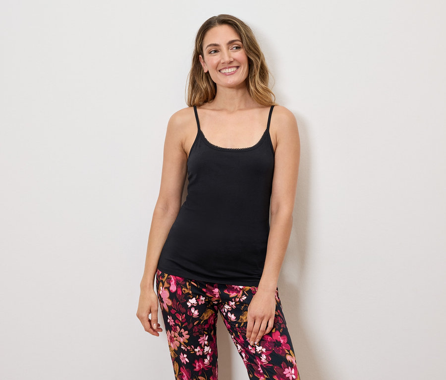 Une femme aux cheveux longs portant un débardeur noir à bretelles et un pantalon à fleurs.