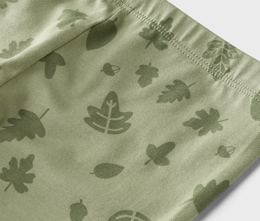 Gros plan d'un pantalon vert clair avec un motif de feuilles et de glands.